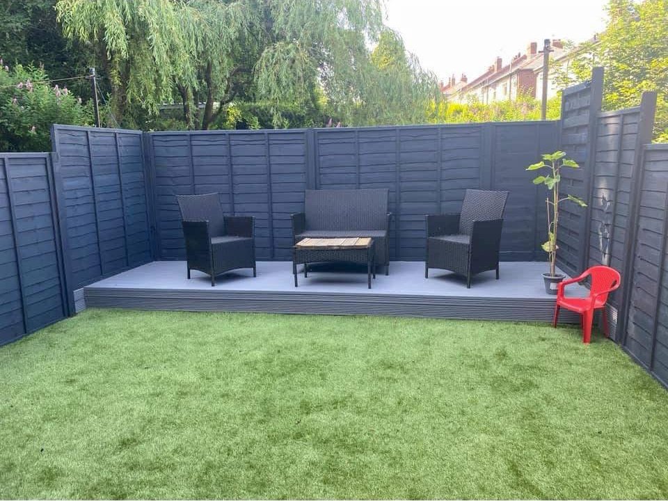 After: garden with new dark fencing, grey raised decking with seating and artificial lawn